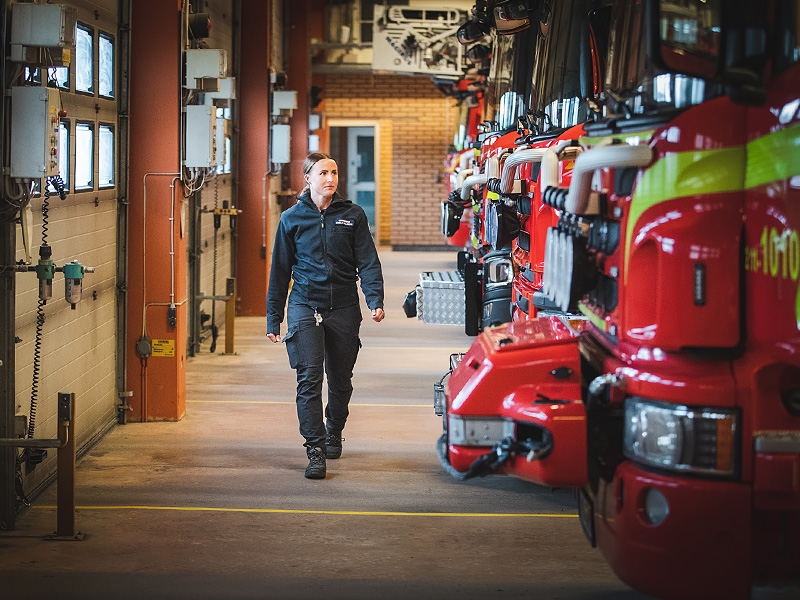 Brandman Emelie går i garaget framför alla brandbilar