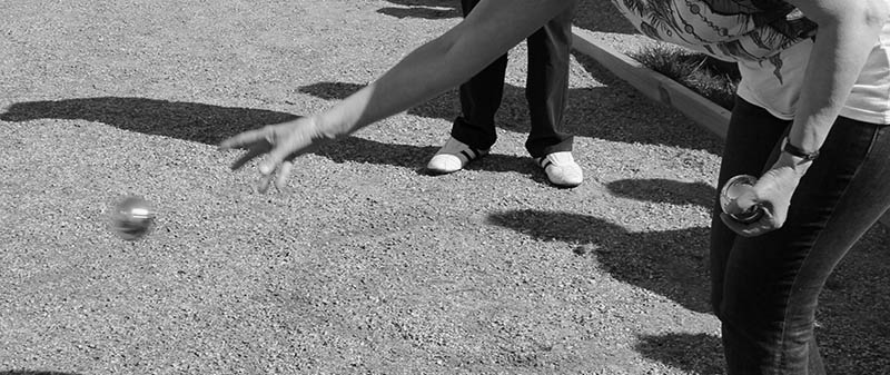 Närbild i svartvitt när två personer spelar boule.