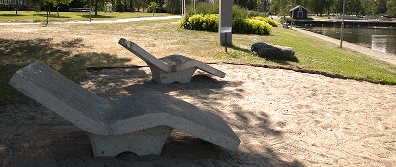 Två solsängar i betong står utplacerade på en liten strand.