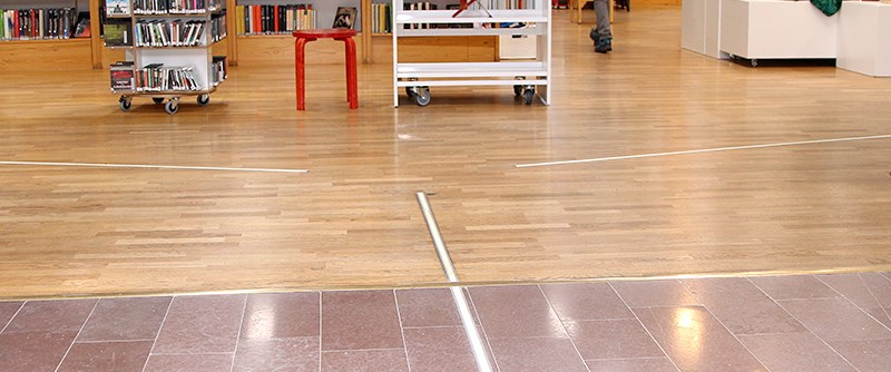 Taktila stråk på Piteå stadsbibliotek guidar synskadade med vit käpp till informationsdisk och talbokshyllor.