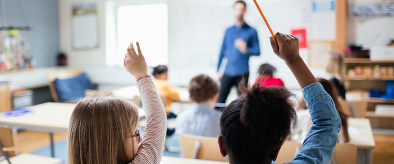 Barn räcker upp handen i ett klassrum